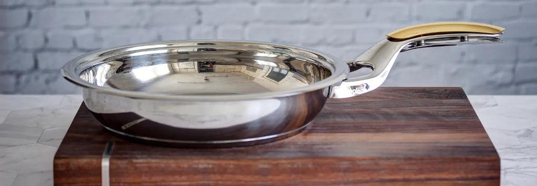 Stainless steel frying pan searing chicken and vegetables on a stovetop in a bright kitchen.