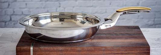 Stainless steel frying pan searing chicken and vegetables on a stovetop in a bright kitchen.
