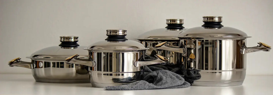 Induction-compatible stainless steel pots and frying pans on a modern kitchen bench